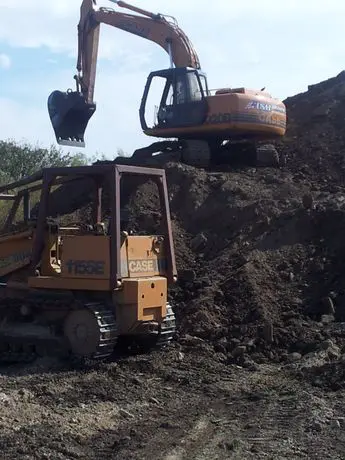 A large dump truck is parked next to the back of a tractor.