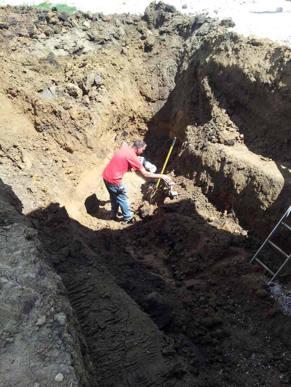 A man in pink shirt digging dirt with shovel.